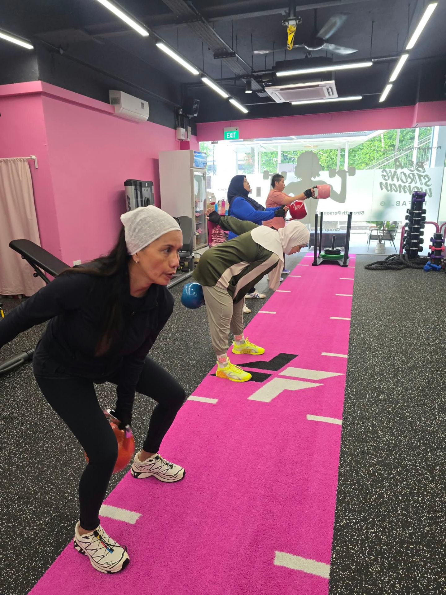 Women practising kettlebell strength exercises at the FitFab.sg pink gym